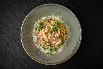 Delicious pasta carbonara with ham and cheese in a ceramic plate on a dark textured background. Restaurant menu Isolated on black