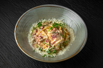 Delicious pasta carbonara with ham and cheese in a ceramic plate on a dark textured background. Restaurant menu Isolated on black