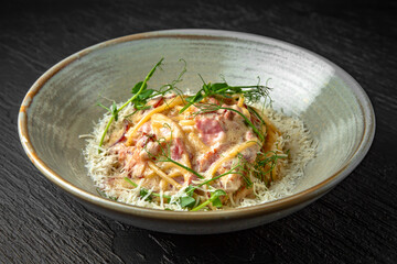 Delicious pasta carbonara with ham and cheese in a ceramic plate on a dark textured background. Restaurant menu Isolated on black