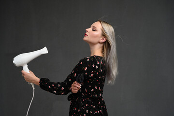 curly blondy woman using hair dryer on gray background. Making perfect curls