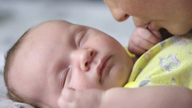 Mother is kissing little hand of her newborn baby. Close up face of the Cute innocent baby and loving mom. 
