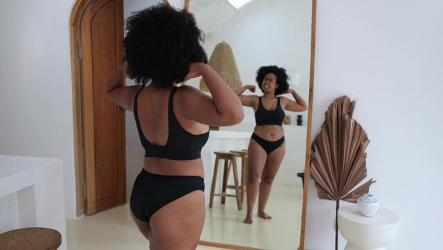 Acceptance of an Afro Asian woman of obesity. A black woman in front of a mirror in black lingerie looks at her magnificent forms and her body likes her. The concept of body positivity.