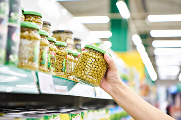 Green peas in glass jar in hands at store