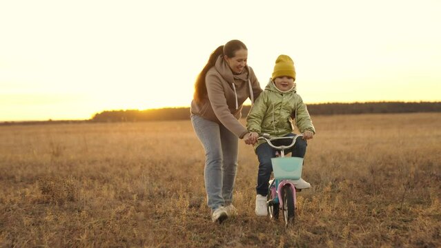 mother teaches little daughter ride two-wheeled bike at sunset, child pedals on bicycle in sunshine, outdoor outdoor activities, exercise at dawn travel, happy family life, childhood dream drive