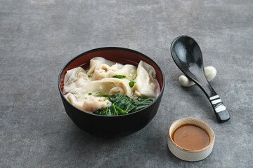 Yummy Wonton Soup (dumpling soup) or Pangsit Kuah served in bowl on dark background.
