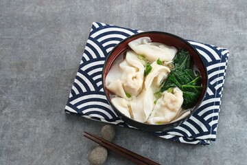 Yummy Wonton Soup (dumpling soup) or Pangsit Kuah served in bowl on dark background.
