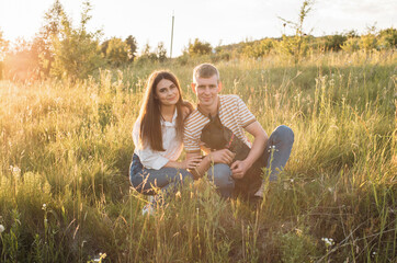 young happy couple having fun with their french bulldog outdoors in the countryside during beautiful sunset