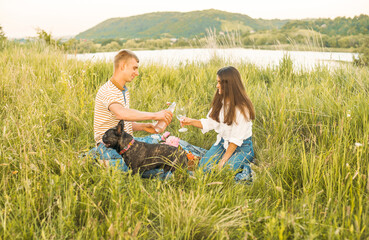 young happy couple having picnic with their french bulldog outdoors in the countryside during beautiful sunset. Romantic date near the lake