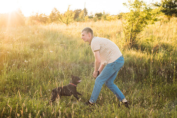 young man playing with his dog outdoors. French bulldog and guy having fun in countryside