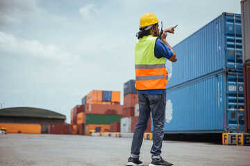 Industrial Engineer checking containers with portable radio in Logistic center. Asian Indian male workers wearing safety vests to working about shipment in Container terminal.