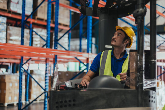 Warehouse worker sitting in vehicle forklift in logistic center. forklift driver wearing hard hat and safety vest to working about shipment in storehouse, Working in Storage Distribution Center.