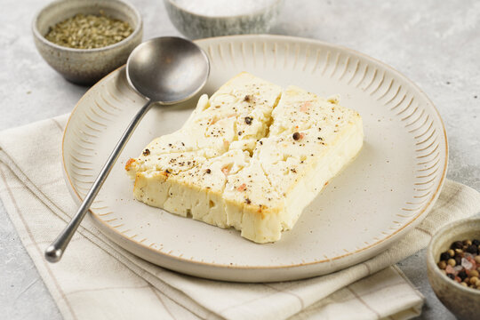 oven baked sheep cheese feta with herbs, oil and spices on round off-white plate, kitchen napkins, grey background