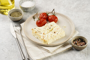 oven baked sheep cheese feta with herbs, oil and spices, roasted tomatoes on branch on round...