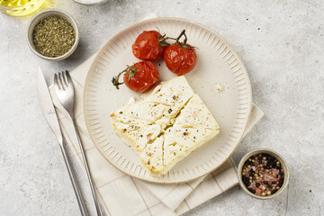 oven baked sheep cheese feta with herbs, oil and spices, roasted tomatoes on branch on round...