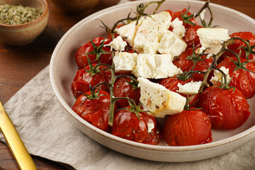 Roasted red tomatoes on branches with seasoned feta cheese on round off-white plate on kitchen napkins on wooden background