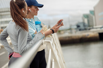 Two young sporty woman standing on bridge and have a rest after morning running in city