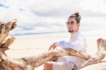 Fototapeta na wymiar オーストラリアのビーチで大木に腕をかけ眩しそうにくつろぐヒスパニック系のサングラスをかけた男性