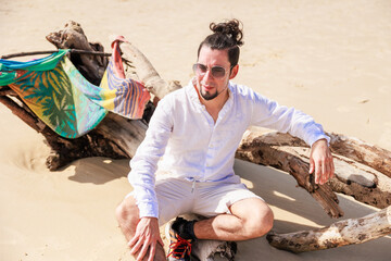 オーストラリアのビーチで大木に腕をかけ眩しそうにくつろぐヒスパニック系のサングラスをかけた男性