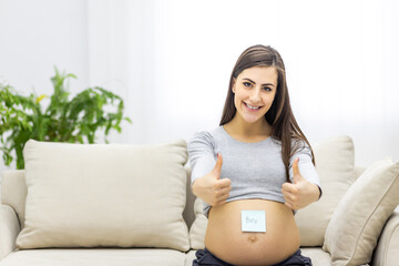 Photo of pregnant woman with blue paper on her stomach showing thumb ups.