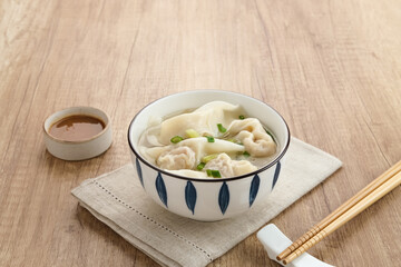 Yummy Wonton Soup (dumpling soup) or Pangsit Kuah served in bowl on wooden background.
