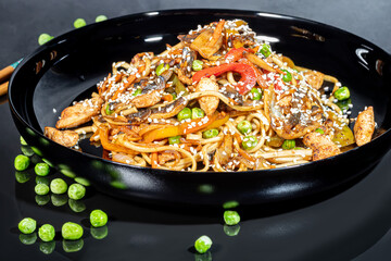 Udon noodles with meat, mushrooms and vegetables. Sprinkled with sesame seeds. Asian food, roast on black background,
