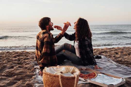 Woman and man eating pizza by the sea, young couple having a picnic and meeting dawn on the beach