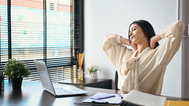 Female employee relaxing at work, reclining back in chair and stretching her arms