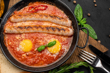 Grilled sausages with tomato sauce and eggs in pan on wooden background