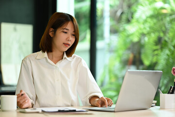 Asian woman manager checking financial data, reading online information on her laptop