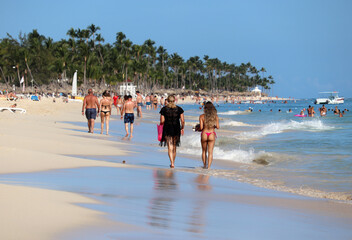 People walking by the sand on coconut palm trees background, girls in bikini in foreground....