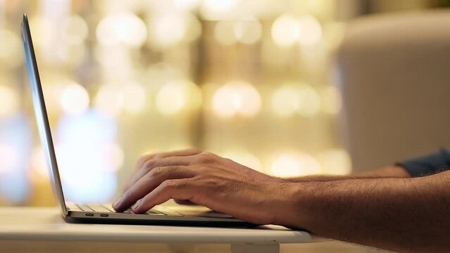Business man hands typing on laptop keyboard on night lights background. Male user remote working late on computer, searching on internet, communicating in web, learning online. Close up side view