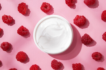 Container with bodycare and skincare cream on a pink background with raspberries. Cosmetic facial skin care and spa. Natural treatment concept.
