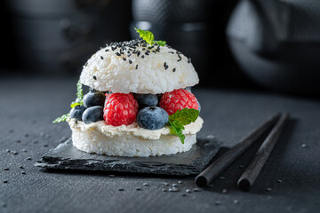 Aromatic sushi burger with sesame and berries on dark plate.