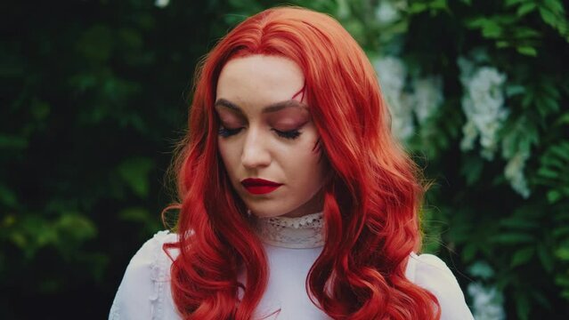 fantasy portrait red-haired woman looking at camera, carnival festive halloween makeup red bloody scratches, wounds, scars on face. Vintage white dress. Summer green garden trees. Gothic vampire girl.