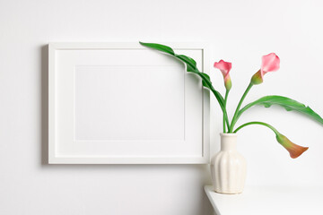 White blank frame mockup on white wall with fresh calla flowers