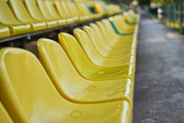 Empty yellow and green plastic seats on stands of stadium in open.