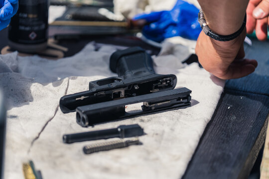 Close up of gunsmith working on handgun broken down into parts lying on rag. Worshop. Horizontal shot. High quality photo