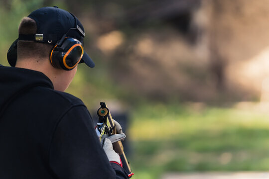 Rear view of man in black hoodie and cap wearing safety headphones reloading gun. Gun training. Firing range. Outdoor horiozntal shot. High quality photo