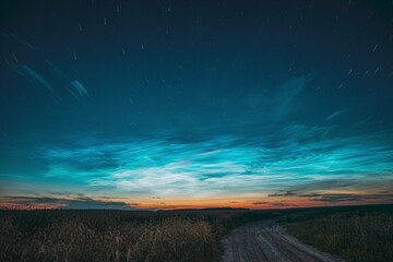 Fototapeta na wymiar Amazing Rotate Stars Effect In Sky. Soft Colors. 6k Unusual Cloud And Stars Effects Above Countryside Rural Field Landscape With Young Wheat Sprouts. Night Blue Sky. , .
