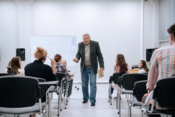 During a physics test in college, a professor in a jacket walks around the audience and communicates with students who write and answer questions