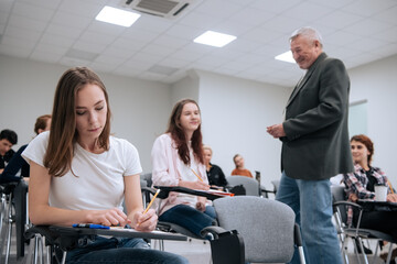 An elderly teacher at a technical university conducts a lecture for first-year students in the college auditorium