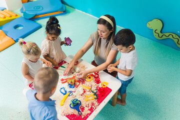 Caucasian teacher and her children making figures from the kinetic sand. High quality photo