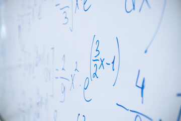 Physical and mathematical formulas written with a blue marker on a white board in a high school...