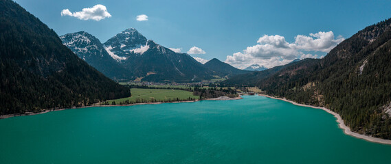 Turquoise colored Lake Plansee with mountains in Tyrol Austria during sunny blue sky weather from above.