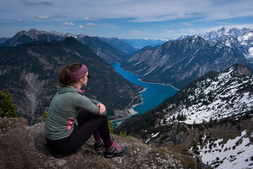 Naklejka na ściany i meble Hiking woman sitting on summit of Zunterkopf with view at Lake Plansee with mountains in Tyrol Austria during sunny weather.