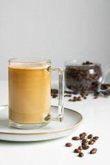 A cup of coffee with milk. In the background is a jar of coffee beans. Close-up.