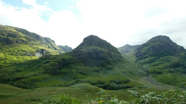 Three green mountain peaks, underneath a cloudy skies in a beautiful summer day. a 4K video clip, Three Sisters of Glencoe, Scotland.