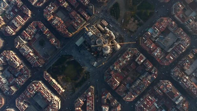 Fly above large unfinished church. Top down shot of famous basilica Sagrada Familia and surrounding blocks of buildings. Barcelona, Spain