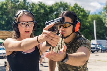 White bearded man instructing caucasian woman how to aim handgun. Safety gear. Firearm training at...