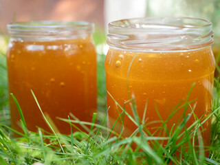 Two glass jars full of fresh amber-colored honey outdoors. Collecting honey